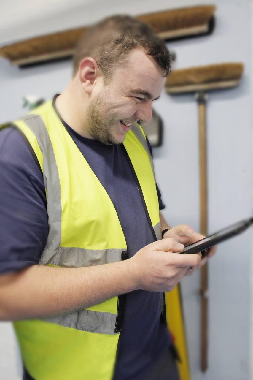 A person in a yellow vest looking at a tablet  Description automatically generated